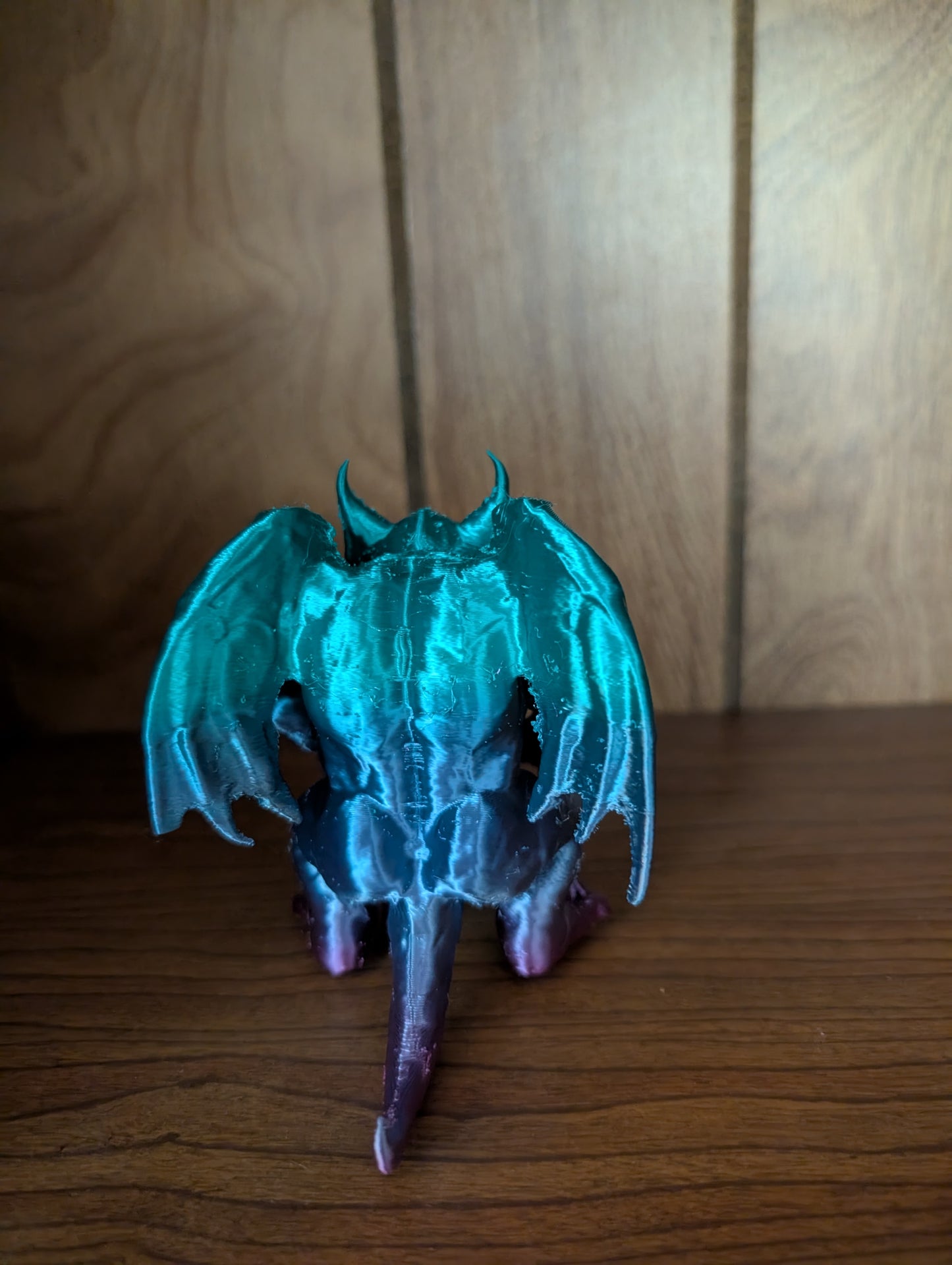 3D printed Beargoyle figurine with teal wings, bear-like body, and purple claws displayed on a wooden shelf.