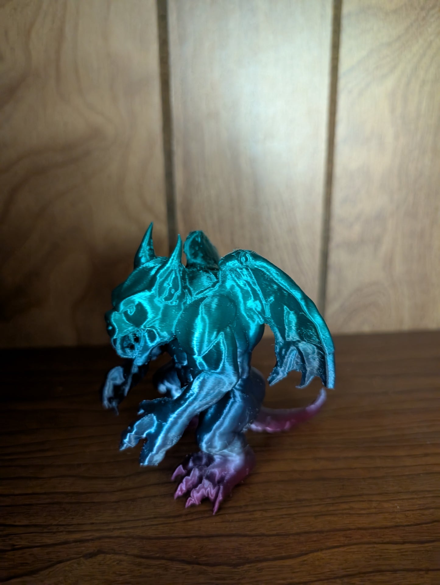 3D printed Beargoyle figurine with teal wings, bear-like body, and purple claws displayed on a wooden shelf.