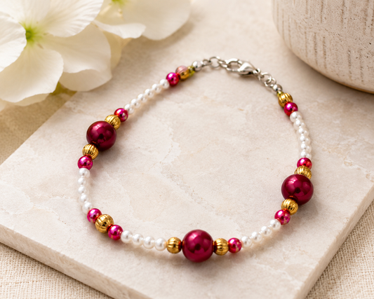 Styled - Elegant handmade pearl and berry bracelet displayed on a neutral stone surface with soft floral decor and warm lighting.