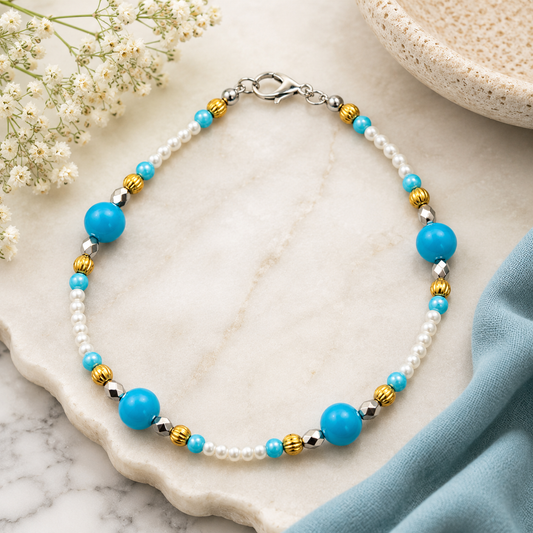 Elegant handmade turquoise and pearl bracelet arranged on a neutral marble surface with soft florals and fabric accents, highlighting the bracelet’s handcrafted detail and vibrant color palette.