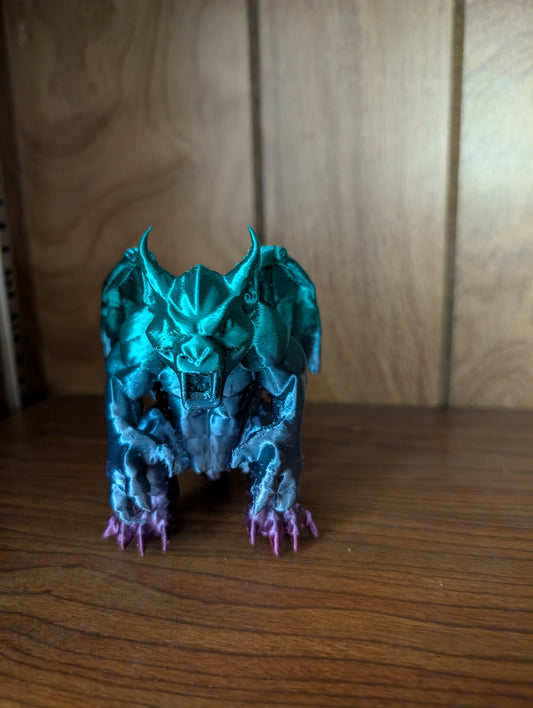 3D printed Beargoyle figurine with teal wings, bear-like body, and purple claws displayed on a wooden shelf.