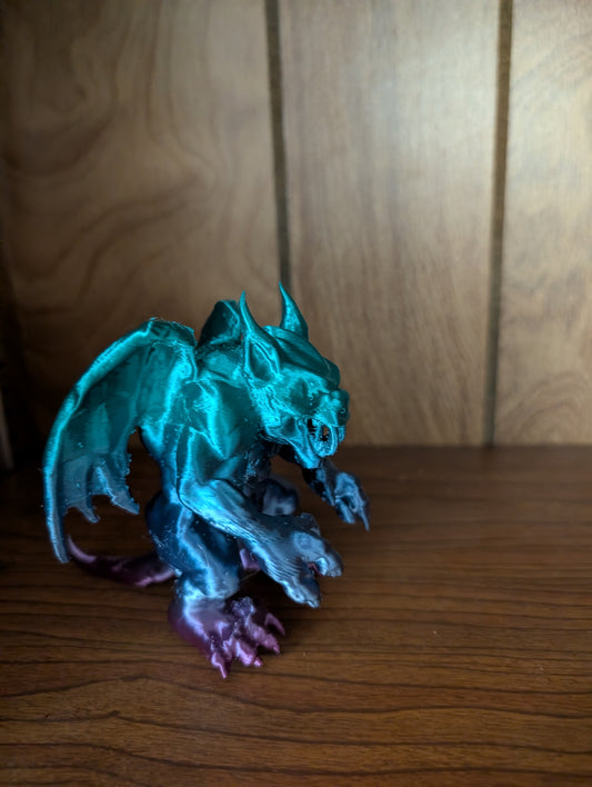 3D printed Beargoyle figurine with teal wings, bear-like body, and purple claws displayed on a wooden shelf.