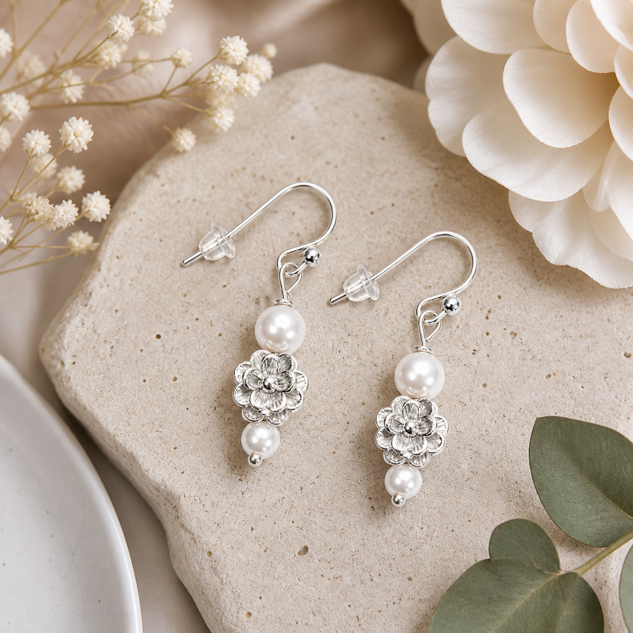 Silver flower pearl earrings styled on neutral stone background elegant feminine jewelry