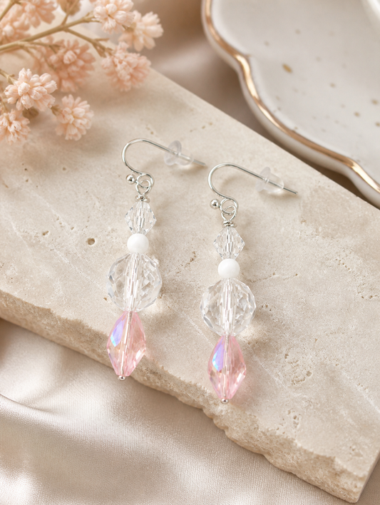 Blush pink and clear crystal earrings styled on neutral stone background elegant feminine jewelry