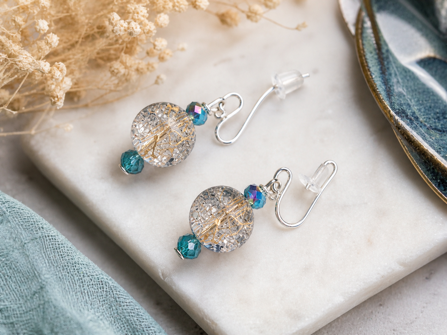 Clear crackle glass earrings with teal accents styled on neutral stone background elegant handmade jewelry