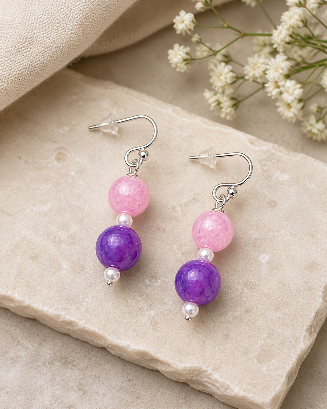 Pink and purple beaded earrings styled on neutral stone background soft feminine jewelry
