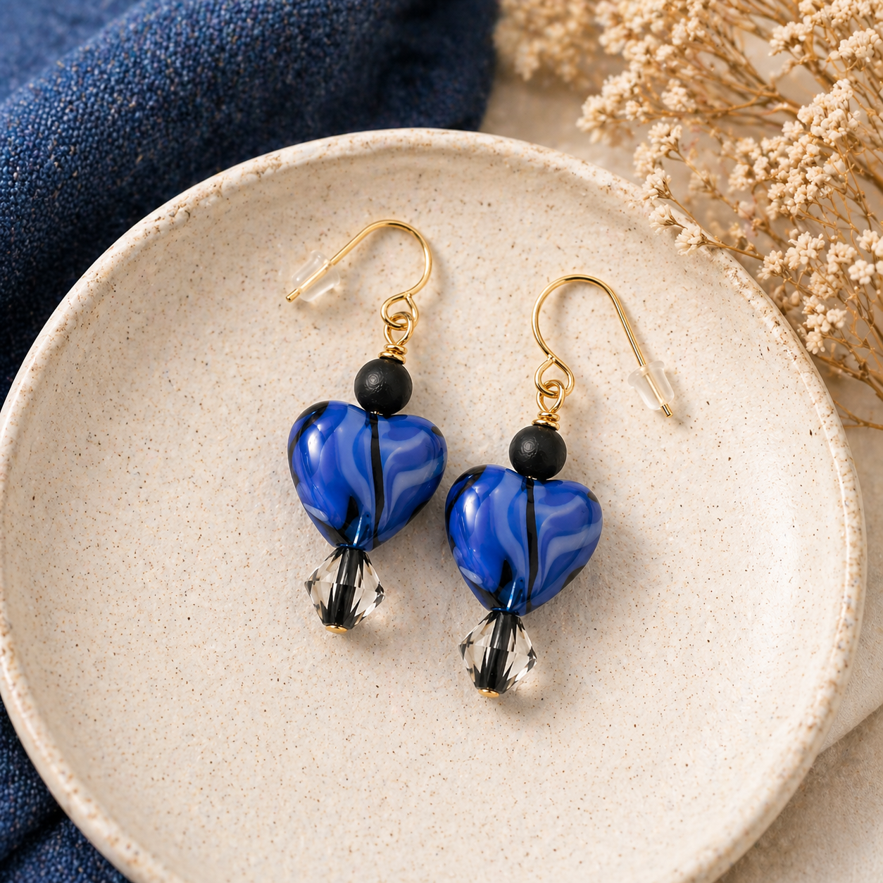 Midnight blue heart earrings styled on ceramic plate with soft background